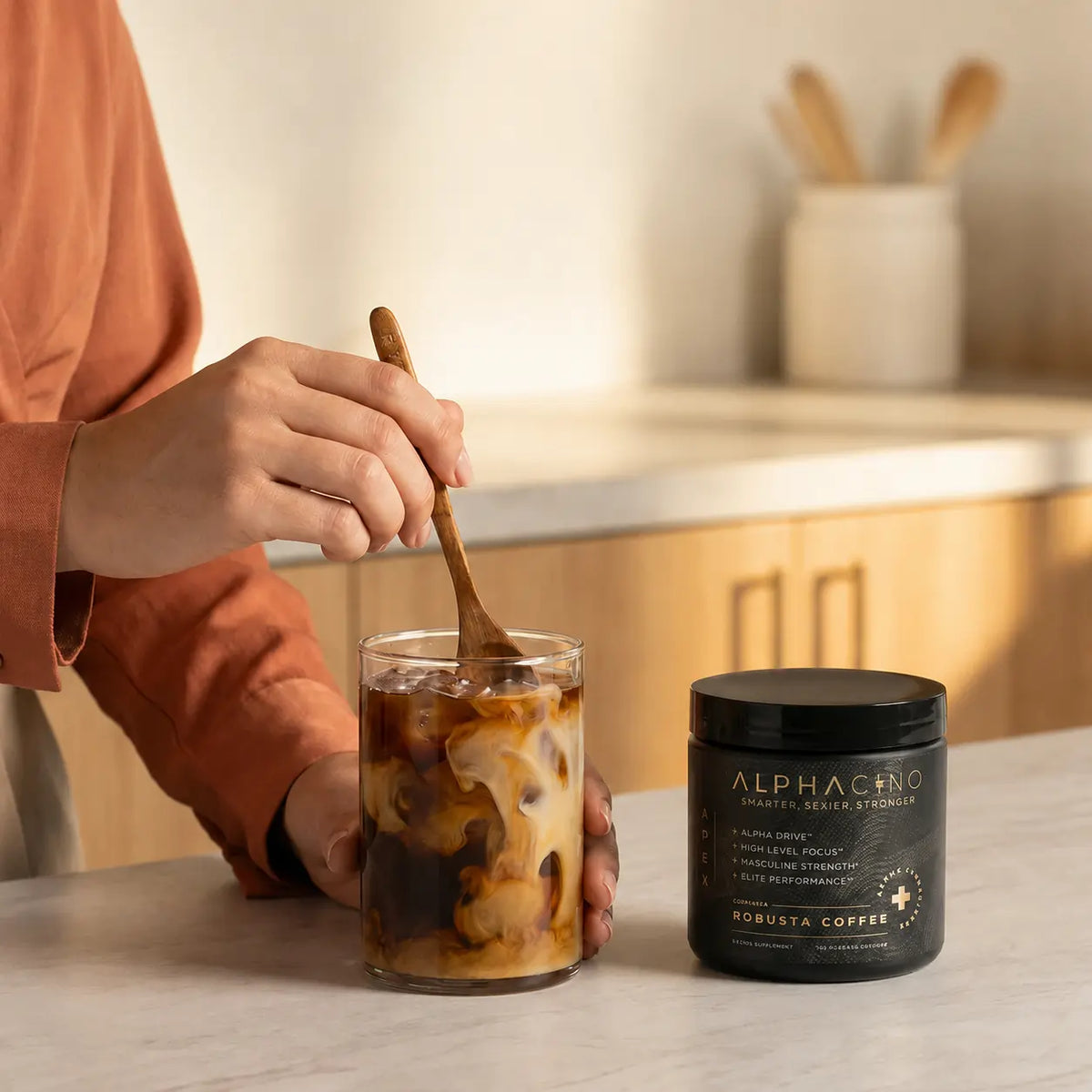 Stirring an iced coffee at a kitchen counter with a jar of Alphacino beside it